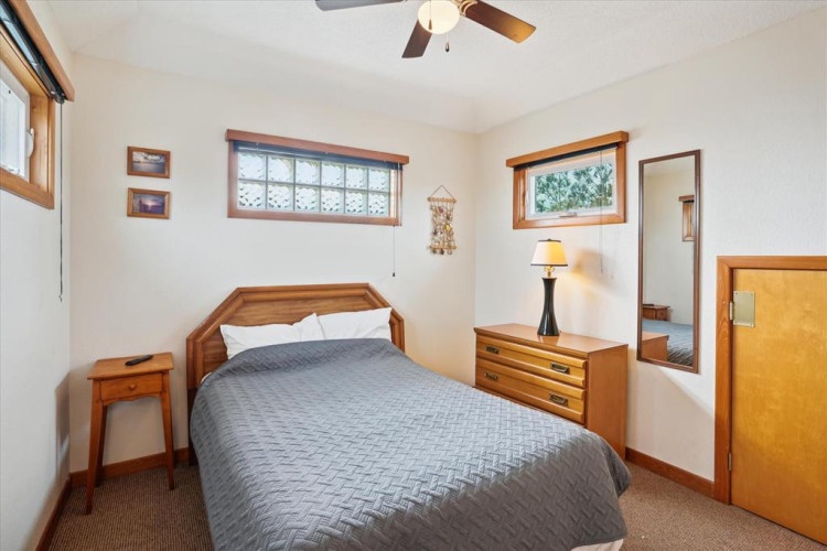Your cozy bedroom features warm wood accents, a plush queen bed, and natural light streaming through multiple windows. Unwind under the ceiling fan after a day of adventure.