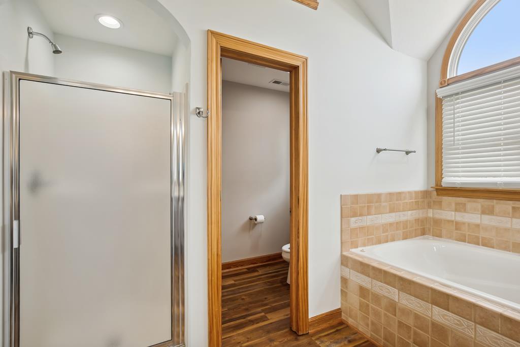Unwind after a long day in your spacious bathroom, featuring a soaking tub with warm tile accents, a glass-enclosed shower, and bright natural light streaming in.
