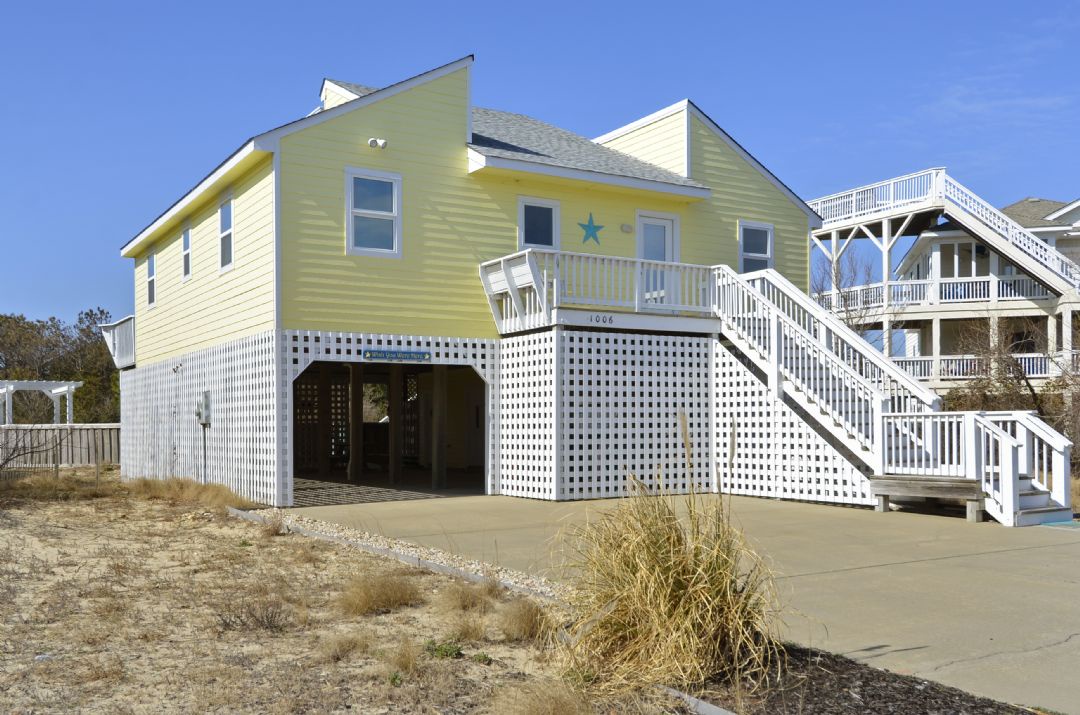 A cheerful yellow beachfront property featuring elevated deck space and convenient covered parking, positioned steps from the sandy shore in a peaceful coastal neighborhood.