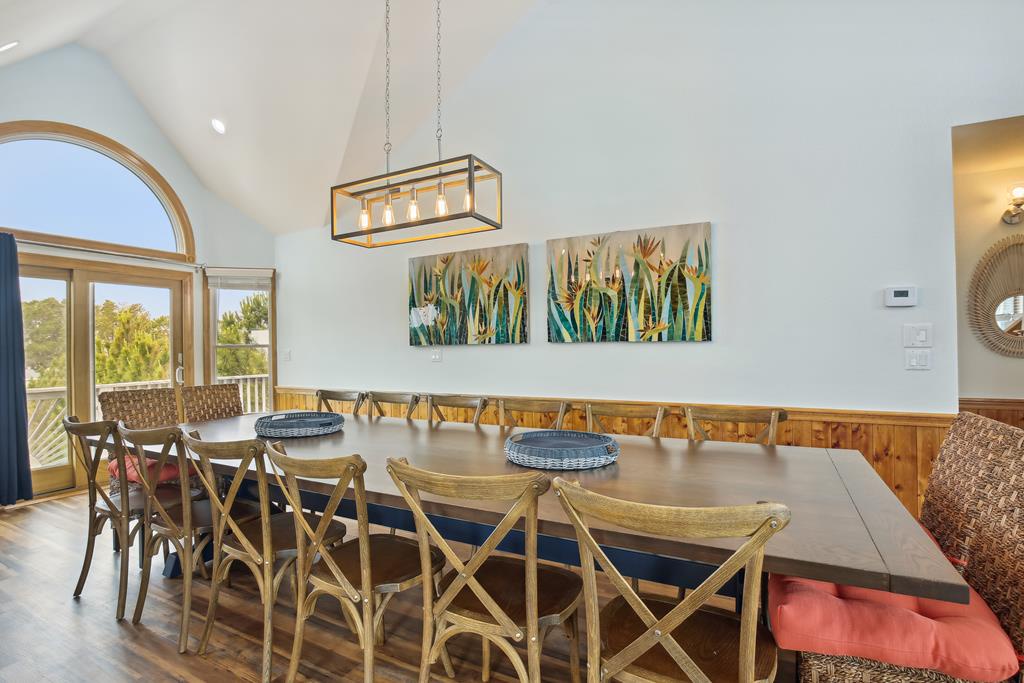 Gather around this inviting farmhouse-style table with seating for ten, where natural light pours through arched windows and coastal artwork sets a relaxed, beachy mood for your group meals.