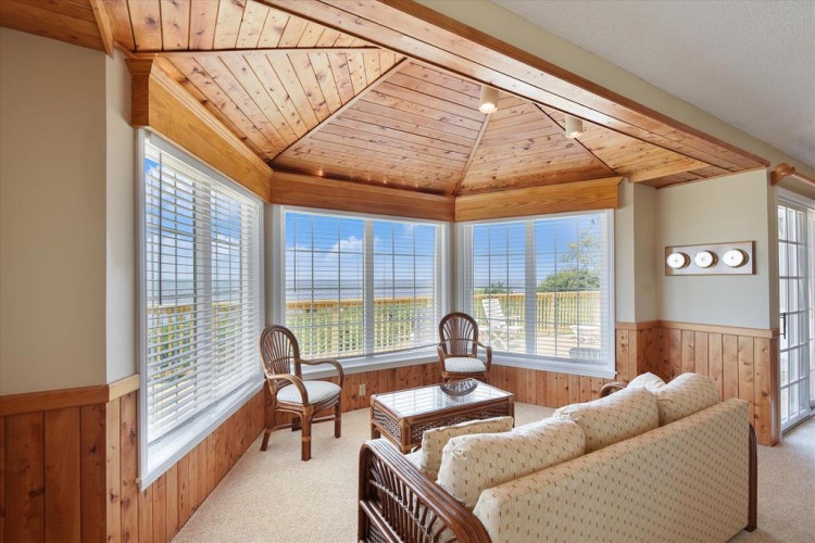 Relax in your sunlit retreat with sweeping coastal views through floor-to-ceiling windows. Cozy seating and warm wood accents create your perfect spot to unwind and soak in the scenery.