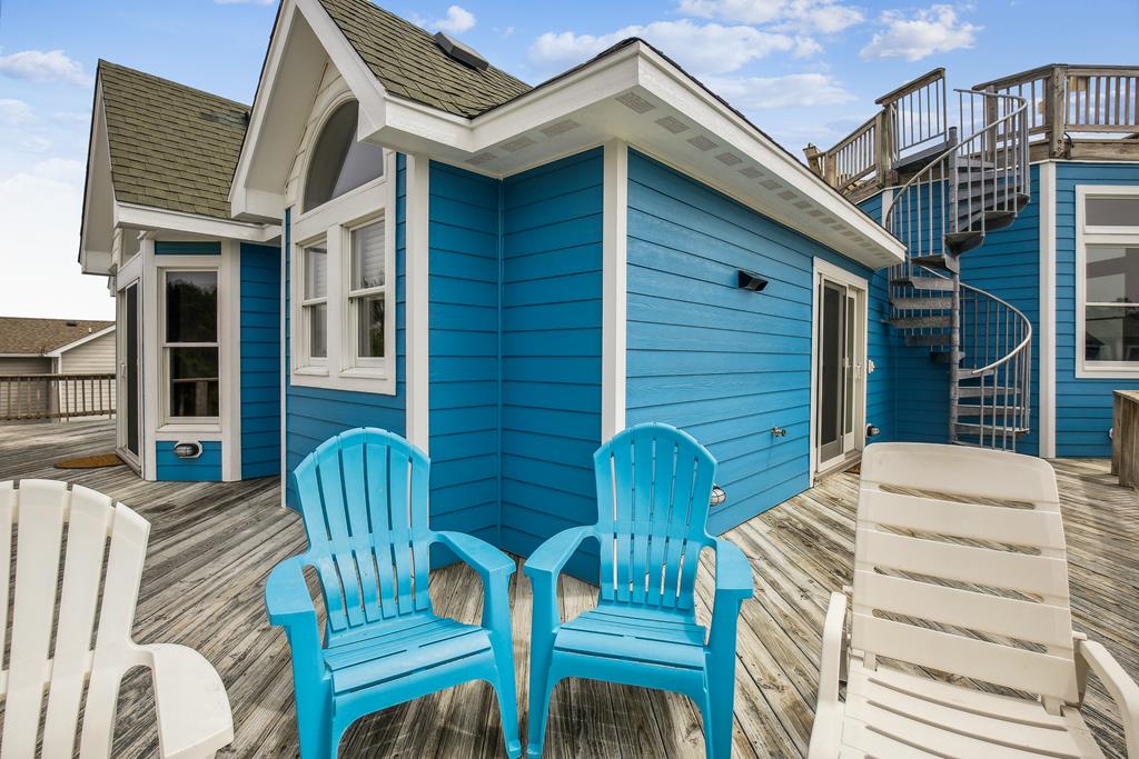 Cheerful blue coastal cottage with bright Adirondack chairs on the deck, blending relaxed beachside living with charming architectural details and easy outdoor access via a spiral staircase.