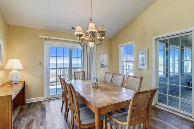Gather around this welcoming dining table where ocean breezes drift through the doors and sunlight streams in, making every meal feel like a beachside celebration.