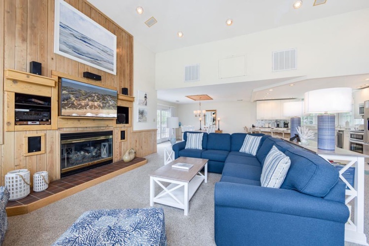 Unwind in your spacious living room with coastal charm, where plush seating and a cozy fireplace invite you to relax after beach adventures, while the open kitchen awaits your culinary creativity.