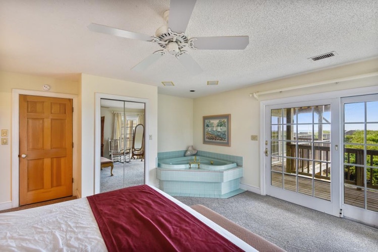 Relax in your spacious suite featuring a private hot tub, ceiling fan, and French doors opening to your balcony with scenic views beyond.