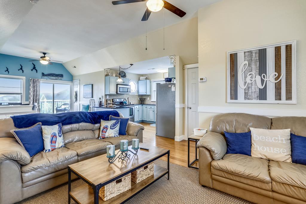 Settle into this inviting open-concept living space where comfortable leather sofas and coastal décor create the perfect retreat for your beach getaway. The airy vaulted ceilings and flowing layout connect living, dining, and kitchen areas.