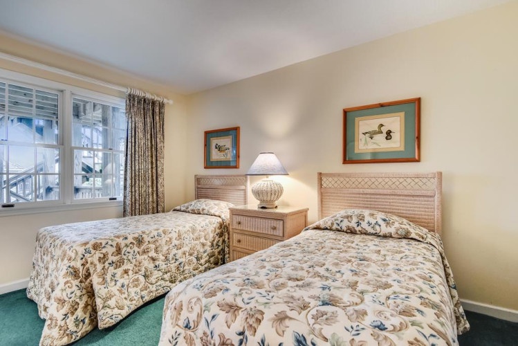 Your peaceful twin bedroom features two comfy beds with classic botanical quilts, duck artwork, and natural light from large windows—perfect for relaxing after a day exploring.