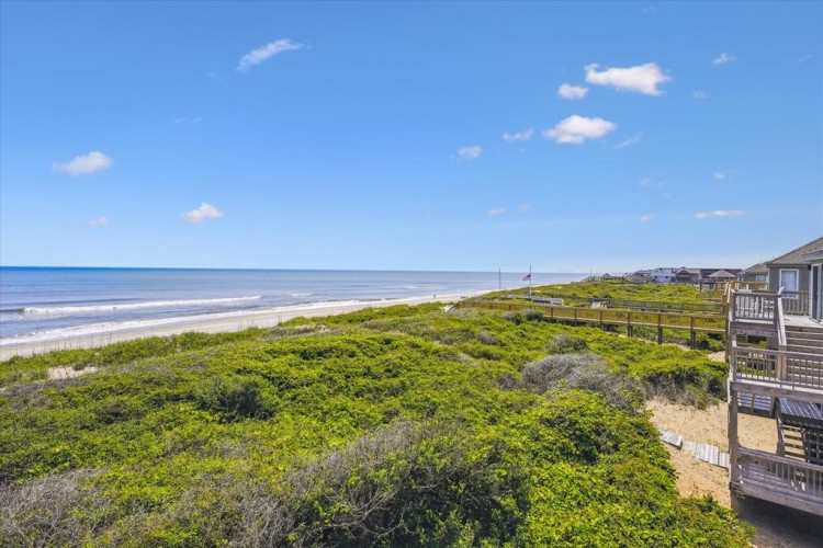 Beachfront property offers direct access to pristine shores via wooden walkway, with sweeping coastal views and lush natural dune vegetation creating a serene seaside setting.