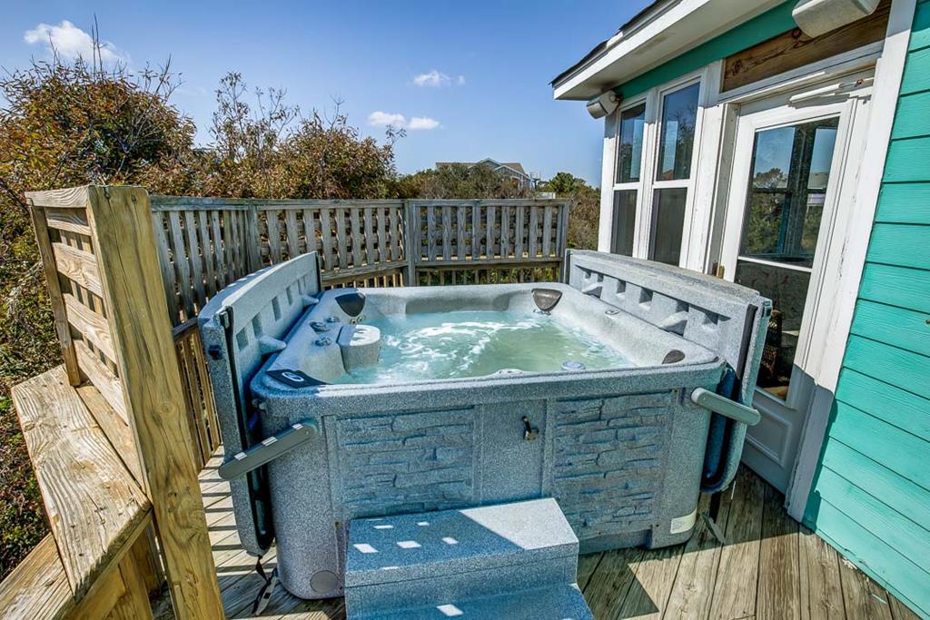 Soak your worries away in your private hot tub on the spacious deck, surrounded by coastal dunes and natural beauty under a bright blue sky.