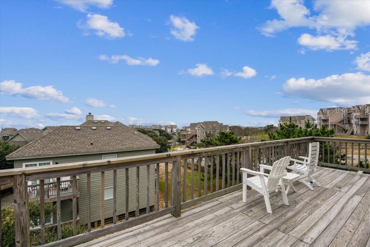 Spacious deck with white Adirondack chairs overlooking a residential coastal neighborhood under blue skies—ideal for morning coffee or evening relaxation.