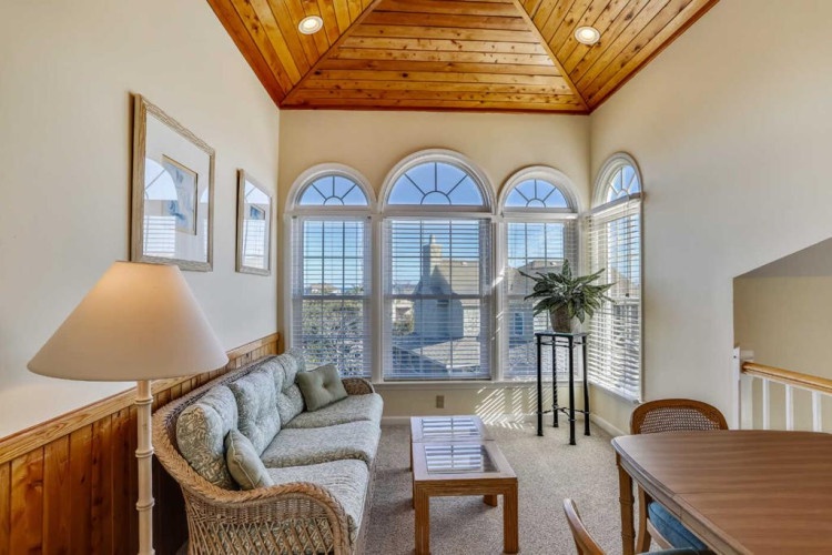 Unwind in this sunlit living space with vaulted wood ceilings, elegant arched windows, and plush seating—your perfect retreat for relaxation and stunning views.