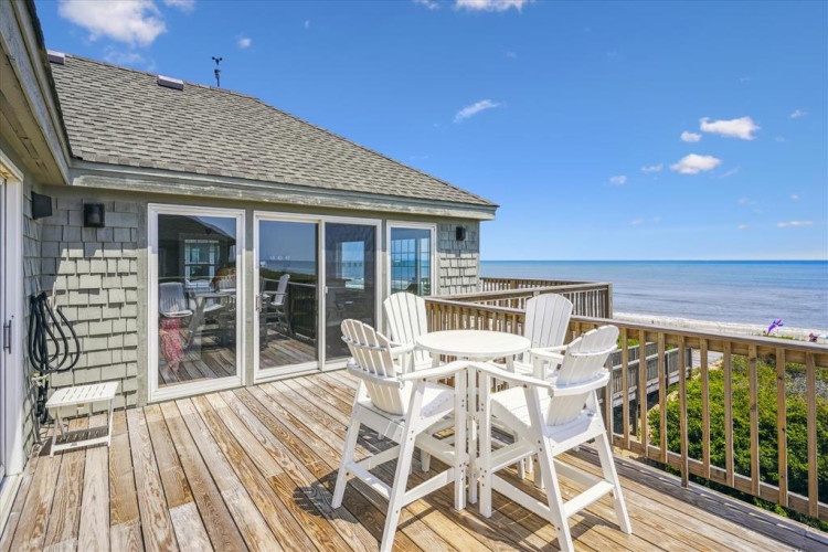 The property features a spacious oceanfront deck with Adirondack seating overlooking the Atlantic coastline. The home sits directly on the beach with sweeping water views and easy access to the shore.