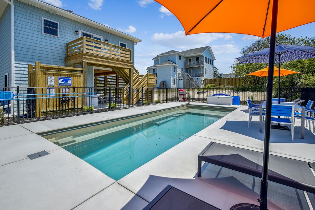 Coastal vacation homes with shared swimming pool, outdoor lounge seating with umbrellas, hot tub, and wooden deck in sunny neighborhood setting.