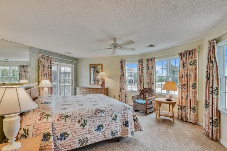 Wake up to natural light streaming through large windows in your peaceful bedroom retreat, where comfort meets coastal charm with a ceiling fan and easy balcony access.