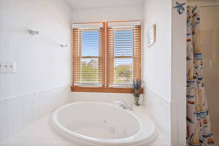 Sink into this spacious jetted tub and let your worries melt away as natural light spills through wooden blinds, framing peaceful views beyond.