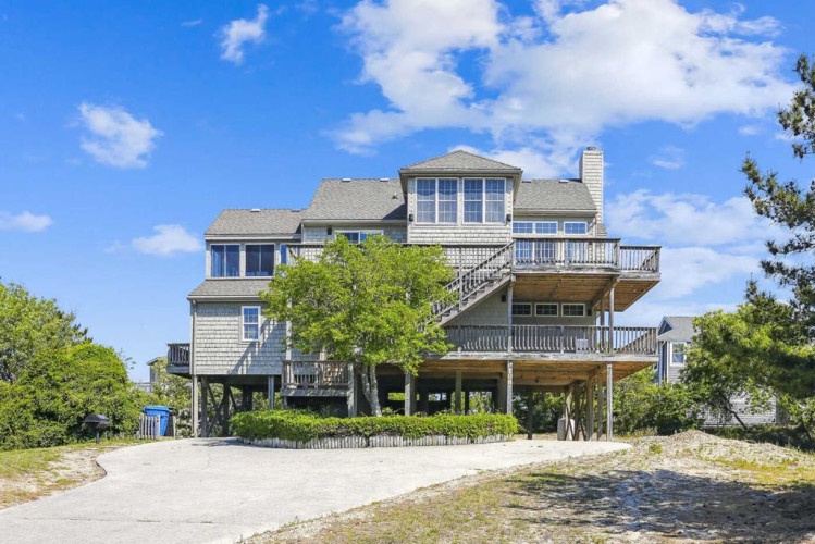 Elevated coastal property with multiple levels of balconies and decks, surrounded by lush greenery and clear blue skies.