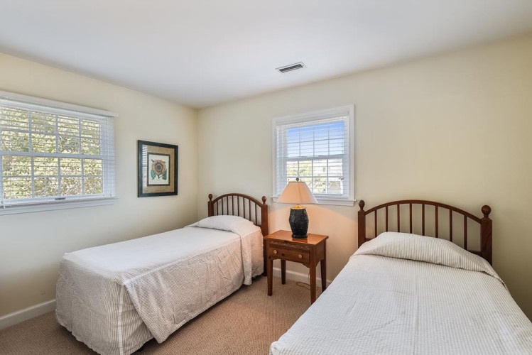 Relax in your bright bedroom with twin beds dressed in soft linens, warm natural light, and a cozy nightstand lamp for evening reading.