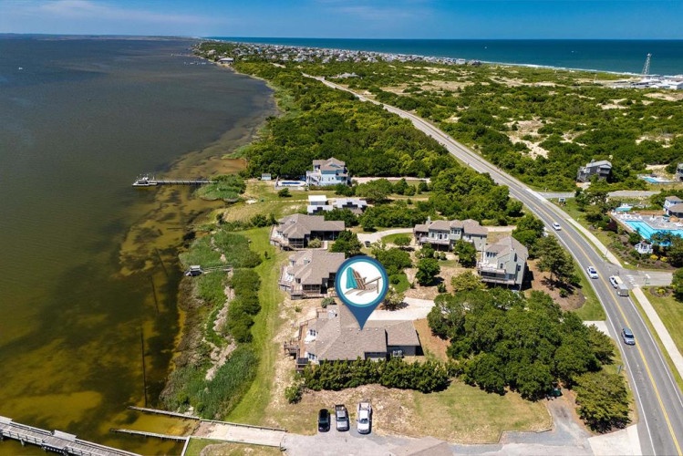 Aerial view of a waterfront vacation rental nestled between bay and ocean, offering peaceful coastal living with nearby beach access and scenic natural surroundings.