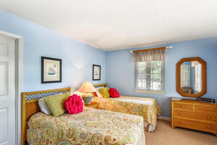 Step into your cozy twin bedroom, where soft blue walls and cheerful paisley bedding invite peaceful nights. Two comfortable beds await, with warm lamplight and coastal artwork creating your perfect seaside retreat.