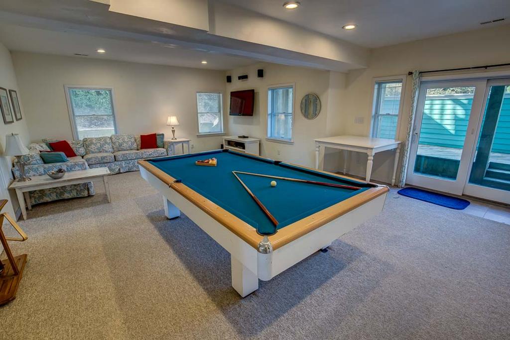 Your private game room invites friendly competition with its full-size pool table, cozy lounge seating, and bright natural light streaming through multiple windows.