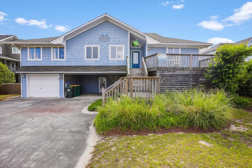 Coastal vacation rental with distinctive blue-gray siding, elevated deck, and convenient parking, situated in a residential beach community under clear skies.