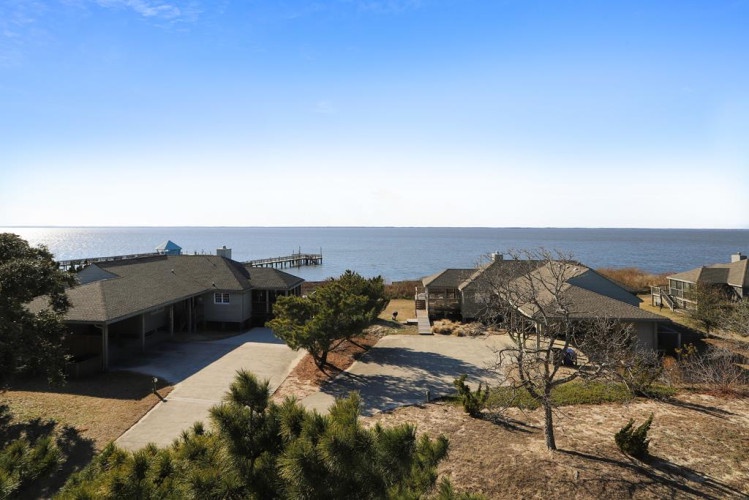Coastal property nestled among natural dunes with direct views of the serene waterfront and nearby pier, offering a peaceful retreat by the sea.