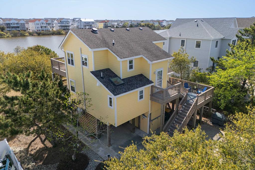 Bright yellow coastal rental home nestled among lush greenery with serene water views, offering spacious decks and a charming neighborhood setting perfect for your beach getaway.