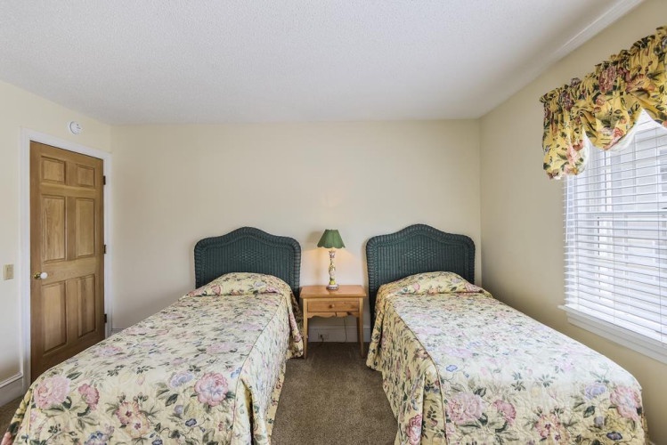 Your peaceful twin bedroom features plush bedding and cheerful floral accents, with natural light streaming through the window to brighten your morning.