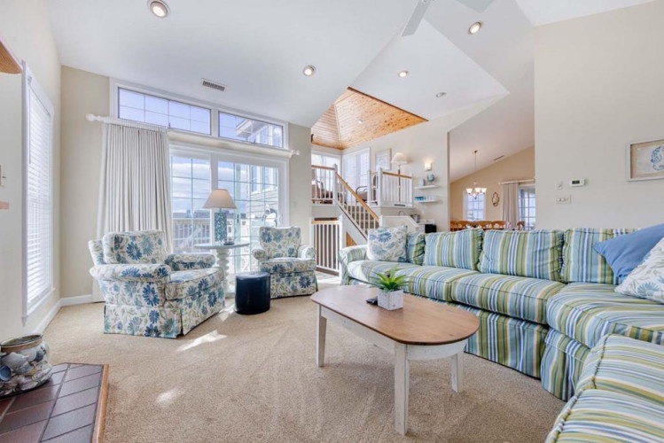 Settle into your coastal-inspired living room, where sunlight pours through soaring windows, illuminating cheerful striped sofas and soft floral chairs. Natural light, vaulted ceilings, and a soothing palette create your perfect beach house retreat.