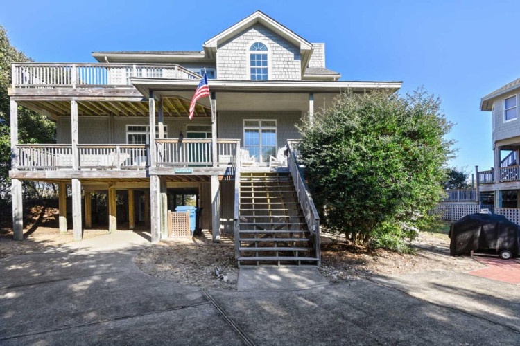 Coastal vacation home with classic shingled exterior, wrap-around porches on multiple levels, and generous parking area—your beach retreat awaits just steps from the shore.