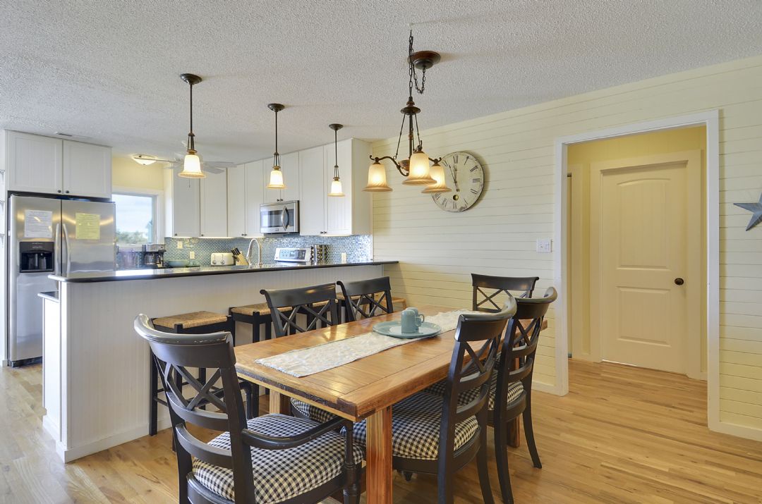 Gather around this welcoming dining table where your morning coffee and shared meals create lasting vacation memories in a beautifully lit, farmhouse-style space.