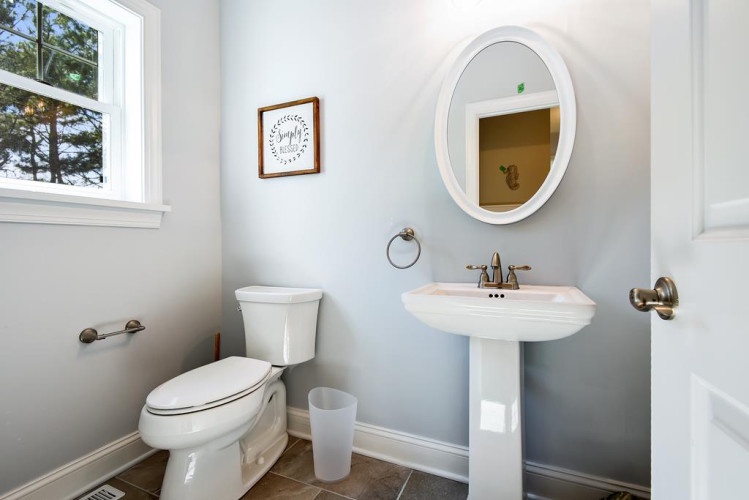 Step into this serene powder room where soft blue walls and warm natural light create a peaceful retreat. The elegant pedestal sink and framed mirror add classic charm to your private escape.