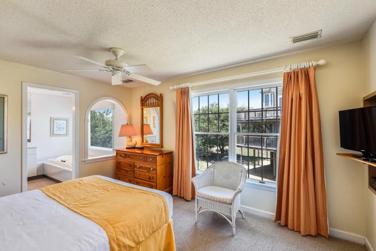 Relax in your bright, coastal bedroom with warm wood furnishings, soft natural light, and a cozy seating nook by the window inviting peaceful mornings and tranquil evenings.