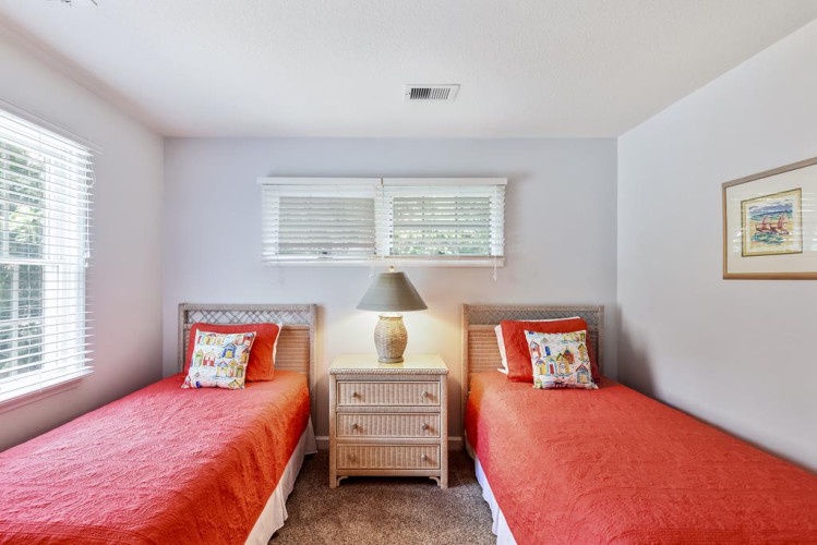 Two twin beds dressed in vibrant coral linens await your arrival, offering a cozy and cheerful space to rest after your adventures. Natural light fills the room, creating a welcoming retreat.