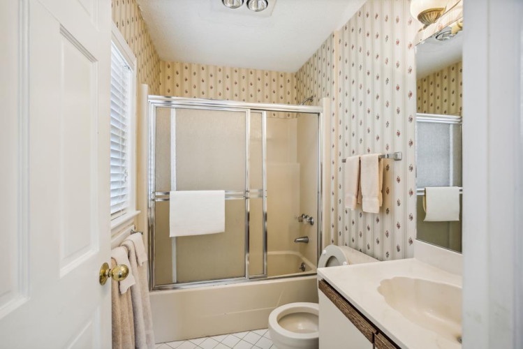 Your private bathroom features a full tub-shower combo with glass doors, dual sinks, and charming vintage wallpaper, offering you a comfortable space to unwind after a day of exploring.