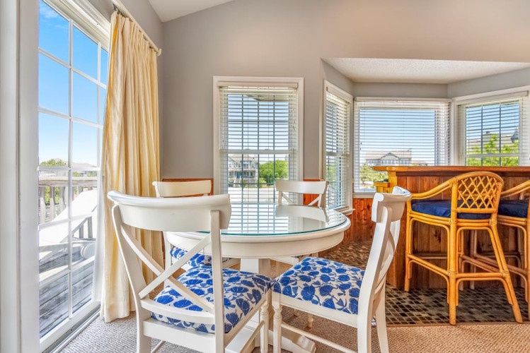 Bright coastal dining area with bold blue-patterned seating, glass-top table, and natural light streaming through your private balcony doors—perfect for morning coffee or casual meals.