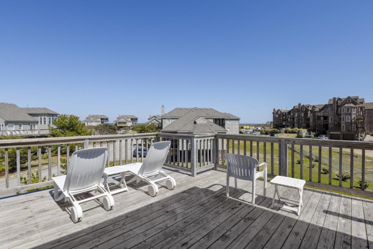 A sun-drenched deck with lounge chairs awaits, offering coastal neighborhood views under clear blue skies—ideal for morning coffee or evening relaxation in your private outdoor space.