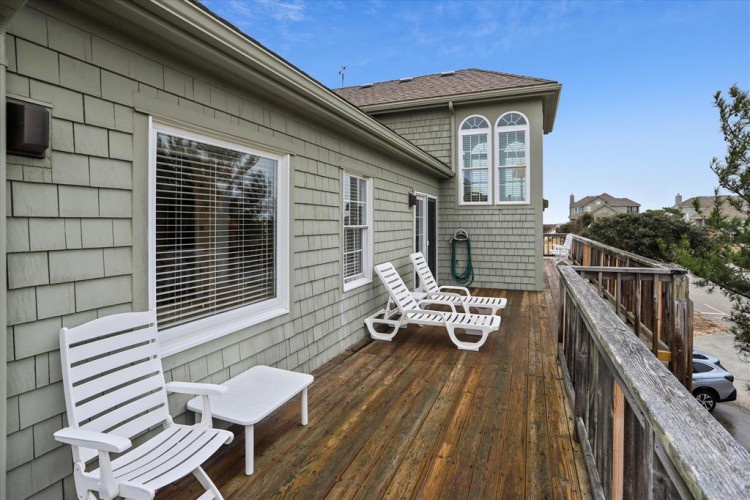 A spacious wooden deck offers the perfect spot to unwind on comfortable lounge chairs, with views of the surrounding neighborhood and clear skies above.