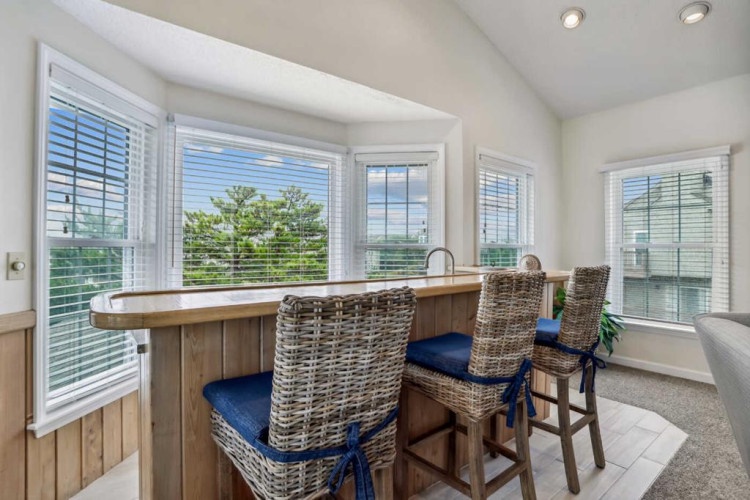 You'll love gathering at this bright breakfast bar with sweeping views of lush greenery through every window. Natural light floods the space, and those woven stools invite you to linger over morning coffee.