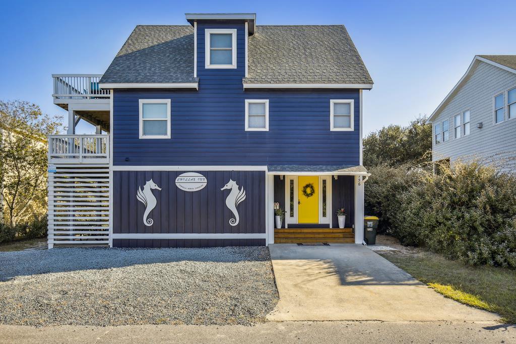 A vibrant blue coastal home with cheerful yellow front door and decorative seahorse accents greets visitors at arrival, with multilevel balconies overlooking the surrounding area.