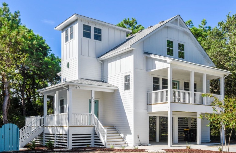A coastal-style vacation home nestled among lush greenery, featuring spacious covered porches and elevated design perfect for enjoying the natural surroundings.