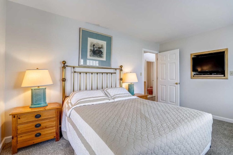 Your restful bedroom features a comfortable bed, soft lighting from bedside lamps, and coastal artwork that sets a relaxing tone for your stay.