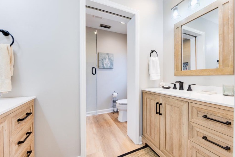 Step into a freshly designed bathroom where warm wood tones meet crisp white surfaces. Your morning routine feels effortless here, with double vanities and a private enclosed area.