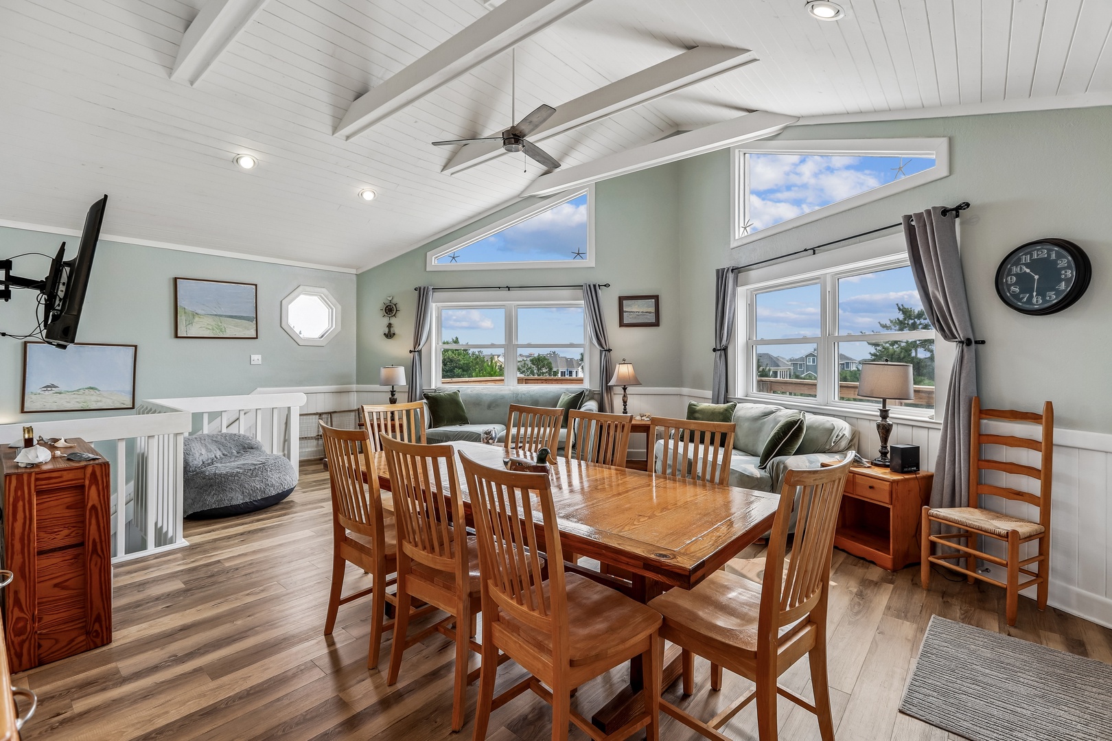 Gather with your group in this bright, open living and dining space with vaulted ceilings, a ceiling fan, and soft natural light streaming through large windows—perfect for meals and relaxing together.