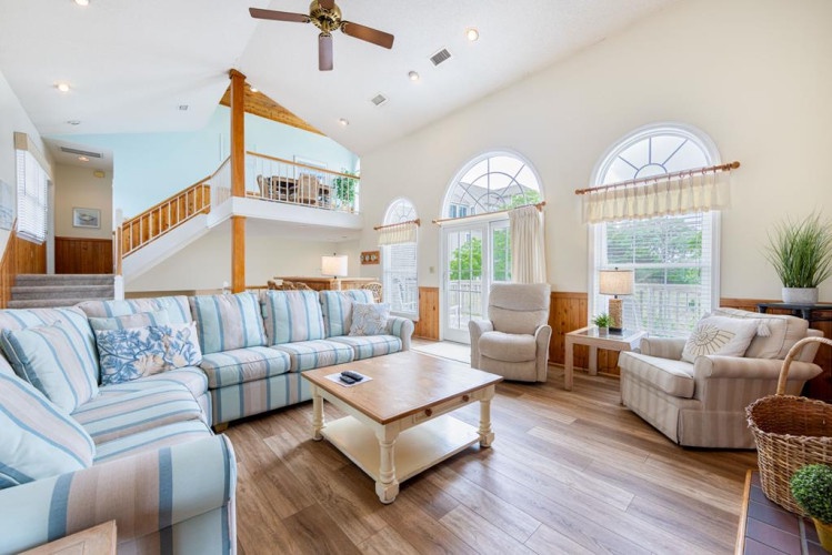 Unwind in this bright, airy living room with soaring vaulted ceilings and coastal charm. Plush seating invites you to relax while natural light pours through arched windows overlooking the outdoors.