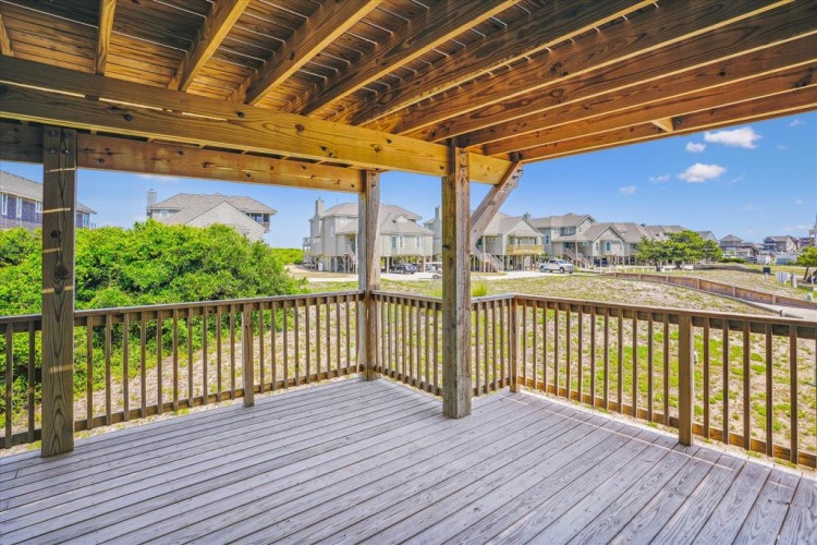 A covered deck overlooks a quiet residential neighborhood with green spaces and nearby homes, providing a shaded outdoor area perfect for morning coffee or evening relaxation.