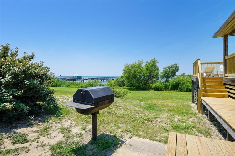 Waterfront rental property featuring a beachside BBQ area, private deck access, and views of the bay and fishing pier.