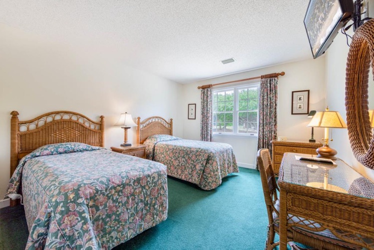 Unwind in this cozy bedroom featuring comfortable twin beds, wicker furnishings, and natural light streaming through large windows. Your peaceful retreat awaits with charming coastal décor and plenty of space to relax.