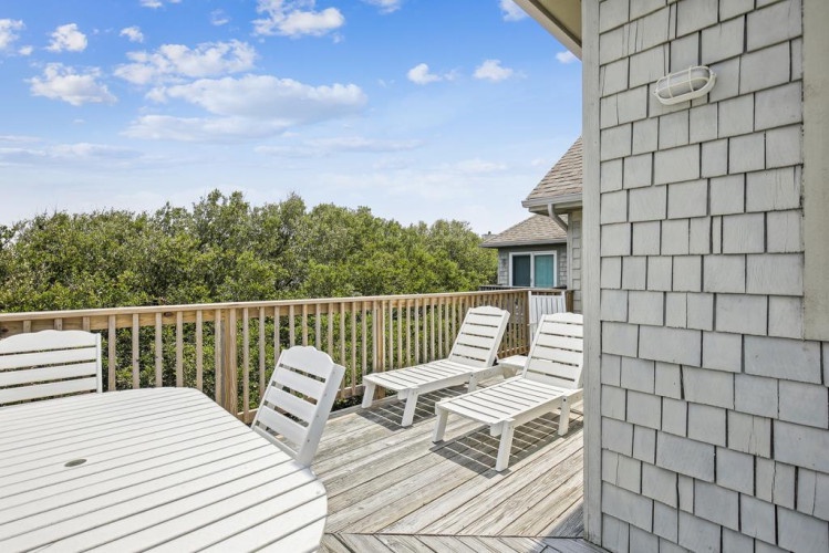A spacious wooden deck offers three loungers for relaxing with peaceful treetop views and clear blue skies stretching overhead.