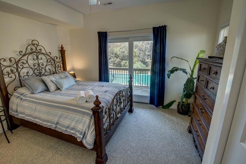 Step into your serene bedroom retreat with plush carpeting, ornate ironwork bed frame, and your own private balcony overlooking a sparkling pool surrounded by mature trees—perfect for morning coffee or evening relaxation.